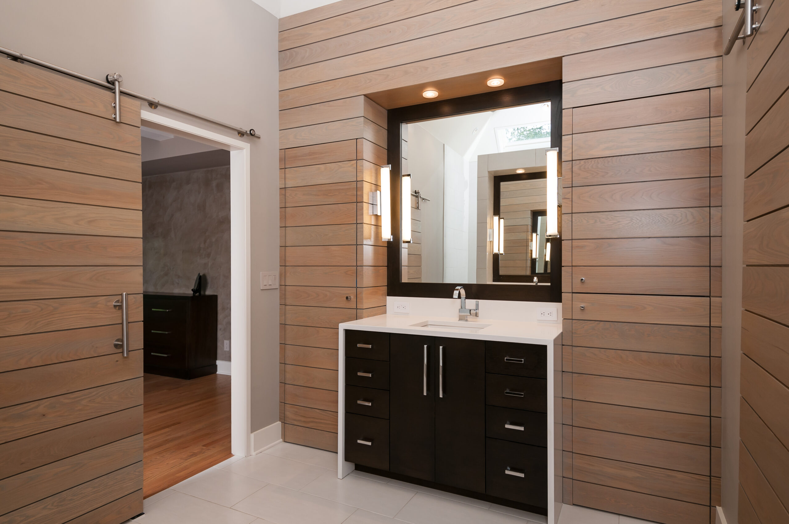 Contemporary primary bathroom with vanity and wood-paneled walls and door