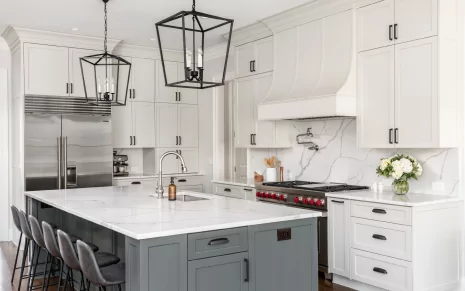 A modern white and gray kitchen with a marble backsplash and counter tops, and two abstract light fixtures hanging over the island.