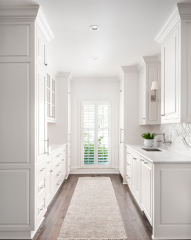 An all white gallery kitchen with cool toned wooden floors and a beige runner.
