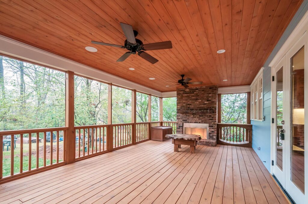 An elevated wooden deck with a stone fireplace and two ceiling fans.