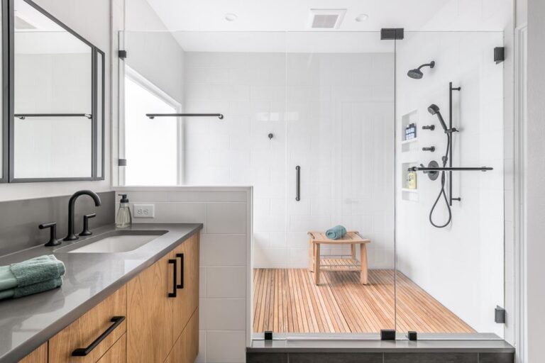 A minimalistic white, gray and light wood bathroom. Next to a sink with a mirror is a large shower with glass doors.