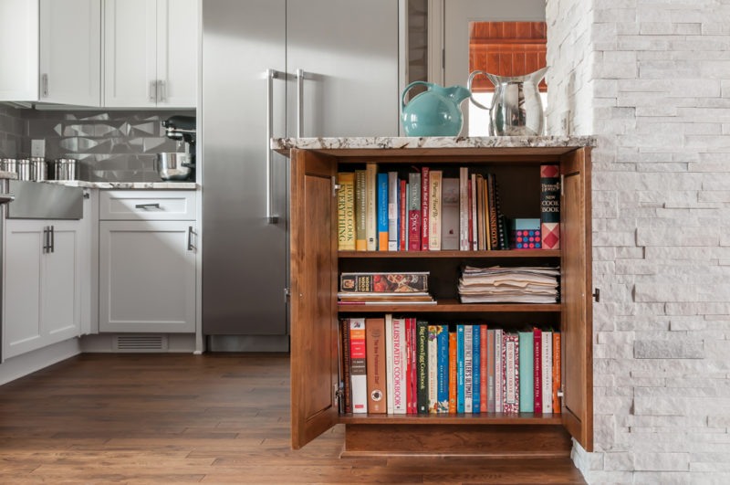 In a mid-century modern kitchen, a white counter is accompanied by a bookcase displaying an assortment of books.