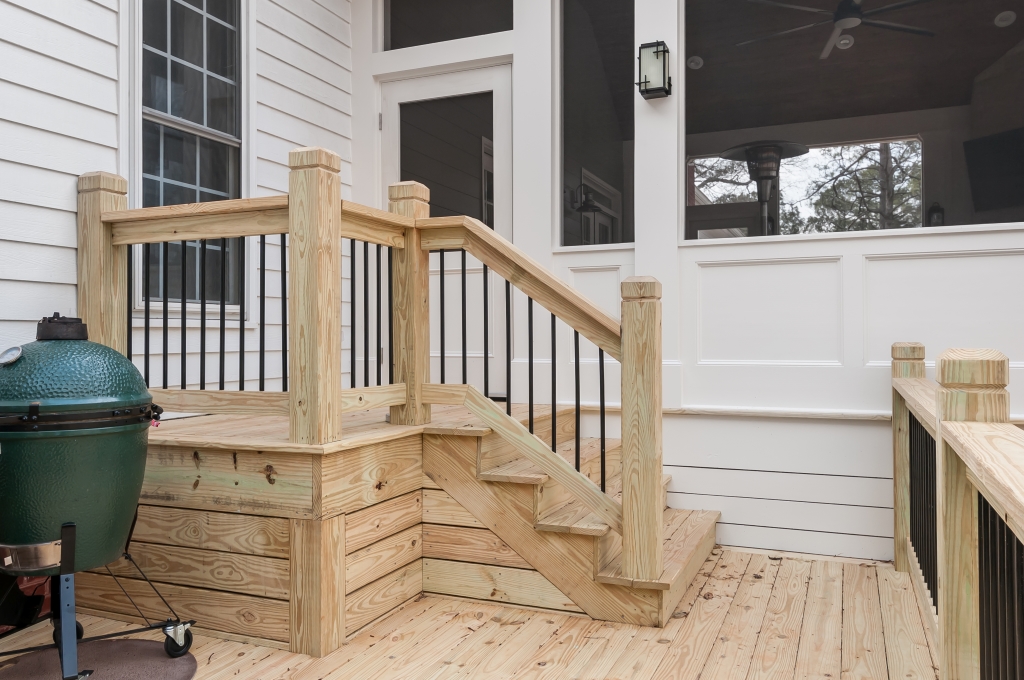 a porch with a grill on the wooden patio and steps leading to the front door