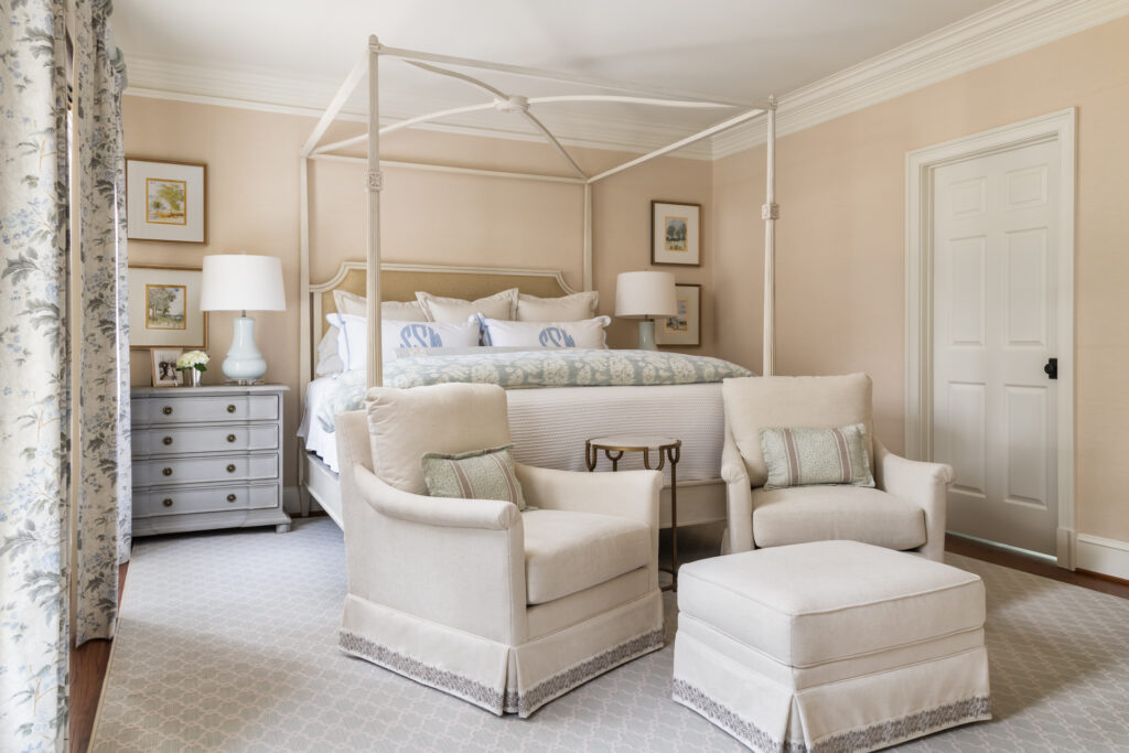 A cream and white bedroom with blue accents. Infront of the bed are two arm chairs and an ottoman.
