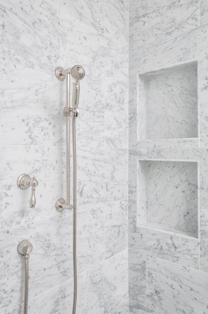 a silver shower head and built in shelving in a walk-in shower