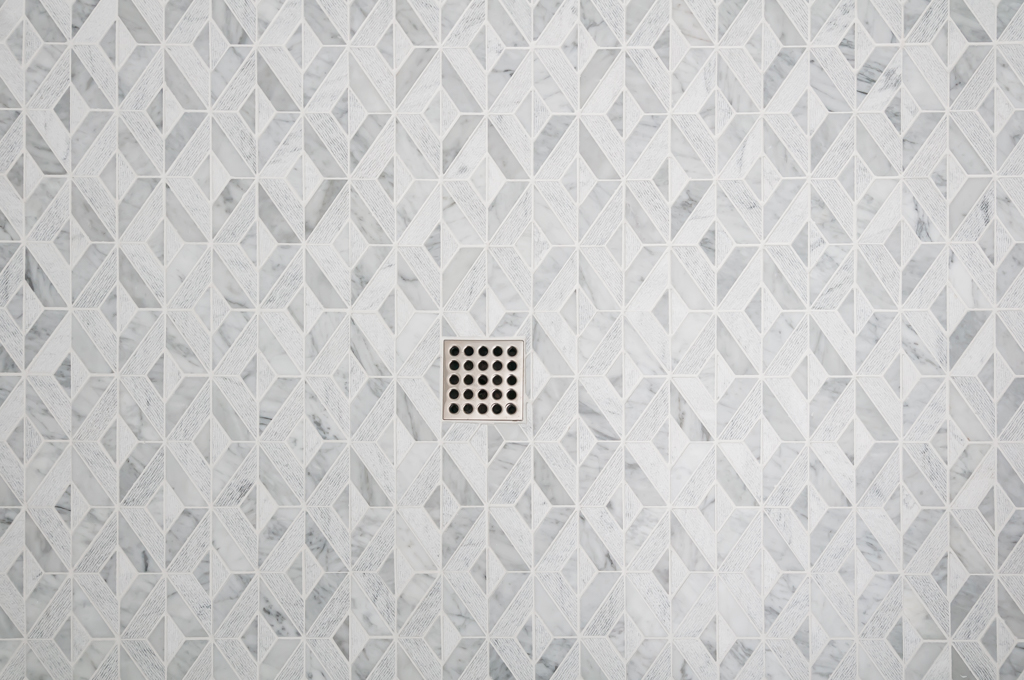 a white tiled shower floor with a square drain in the middle