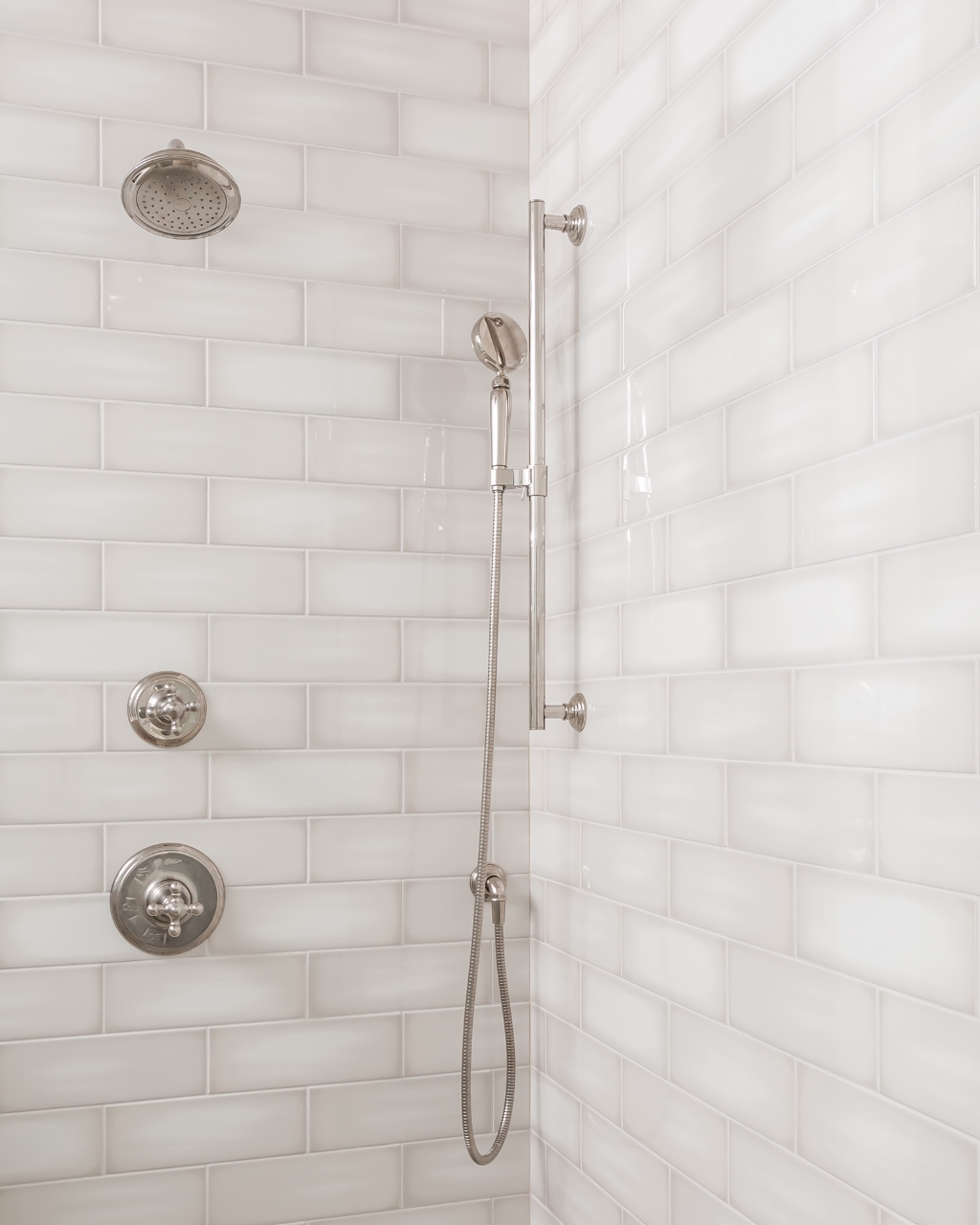 a shower head and handset in a white tiled bathroom