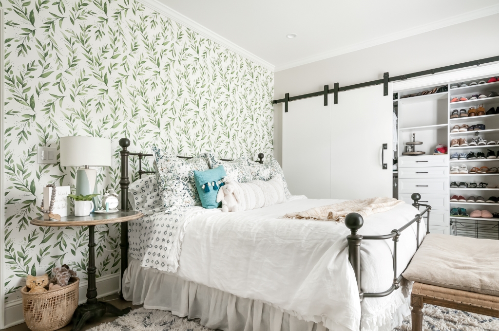 a bedroom with a plush white bed, built in organizers in the closet, and green wallpaper