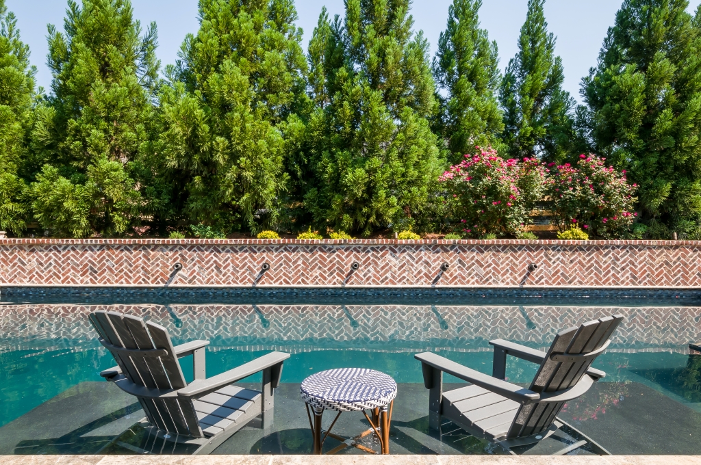 two outdoor chairs sitting next to a swimming pool in an upscale backyard