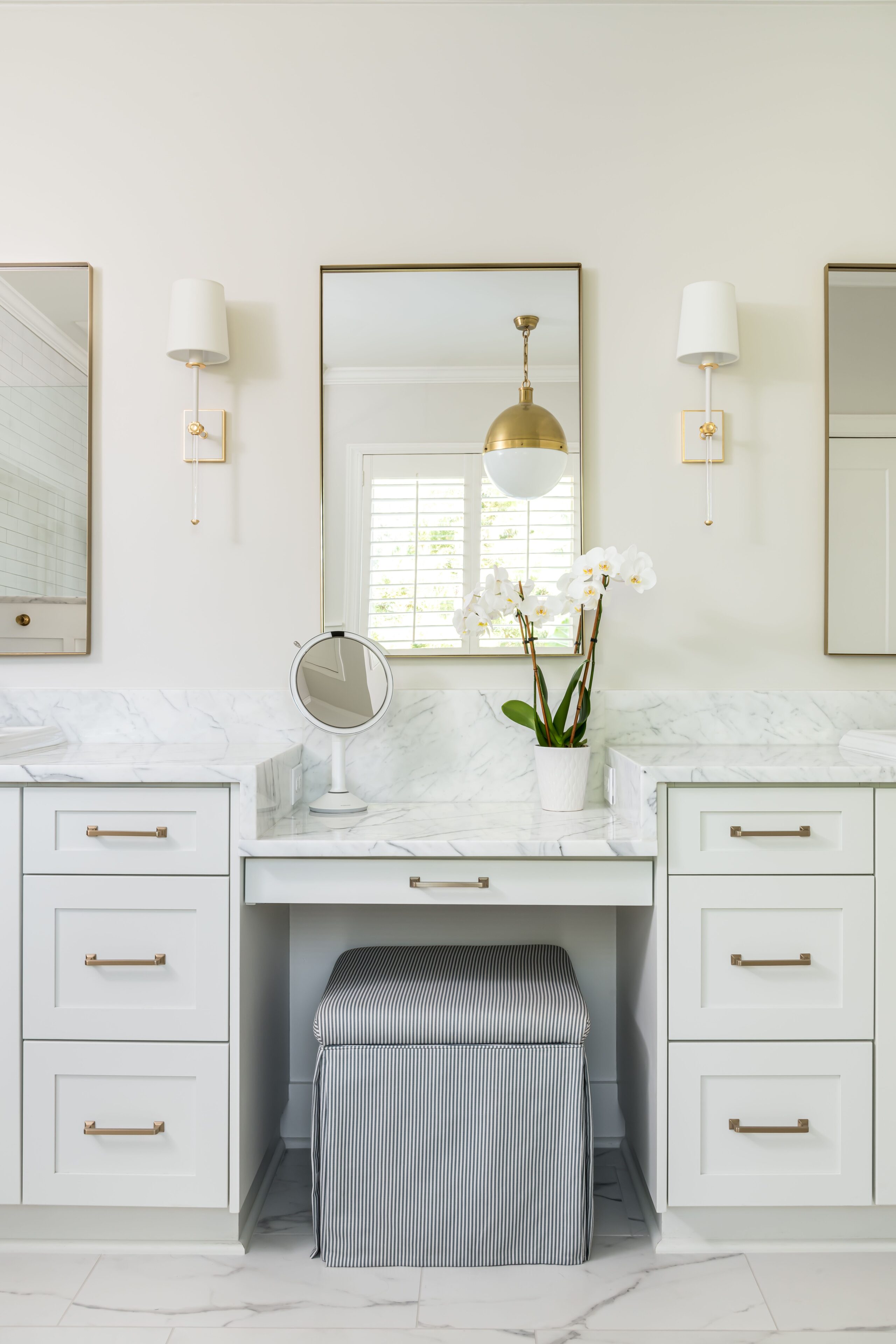 a white bathroom with marble counter tops and gold accents