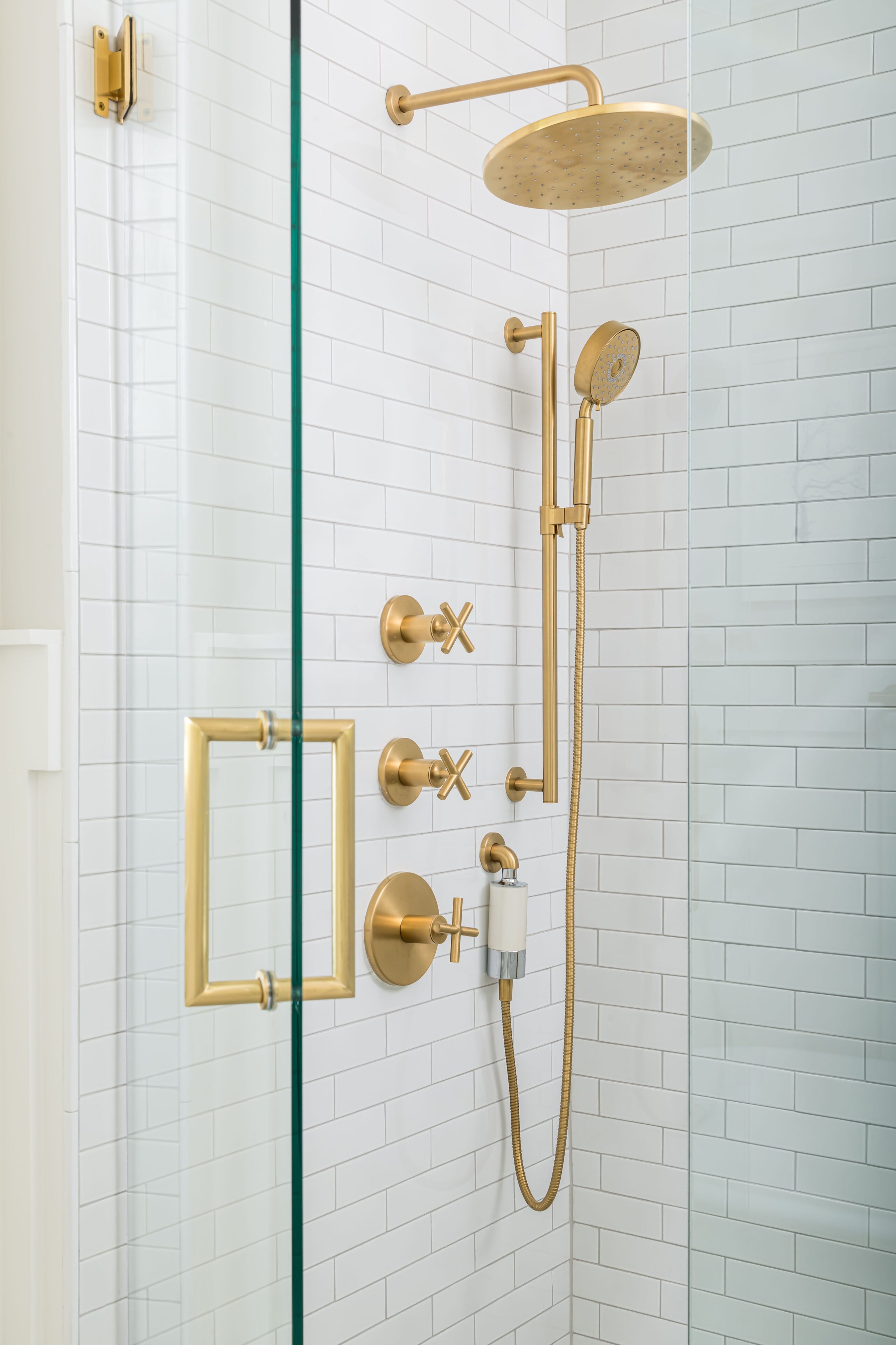 a shower with gold fixtures and white tile