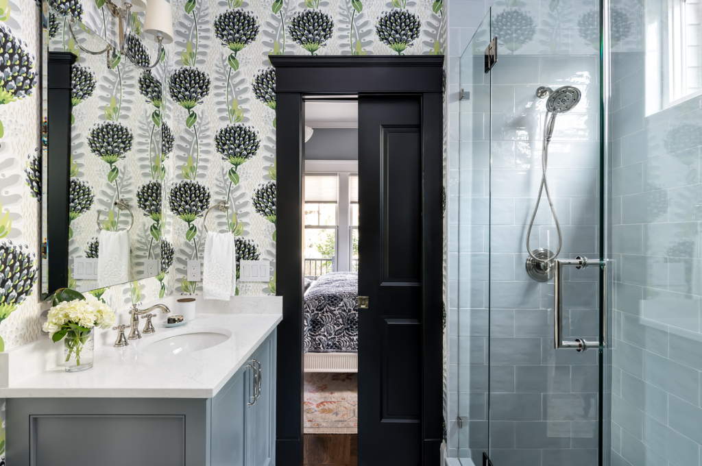 A newly remodeled bathroom with green floral wallpaper and blue cabinets and tiles.