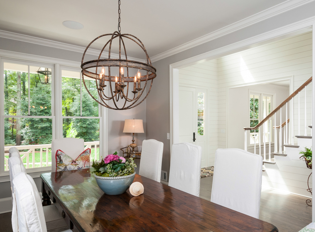 a dining room table with white chairs, a unique chandelier, and large windows