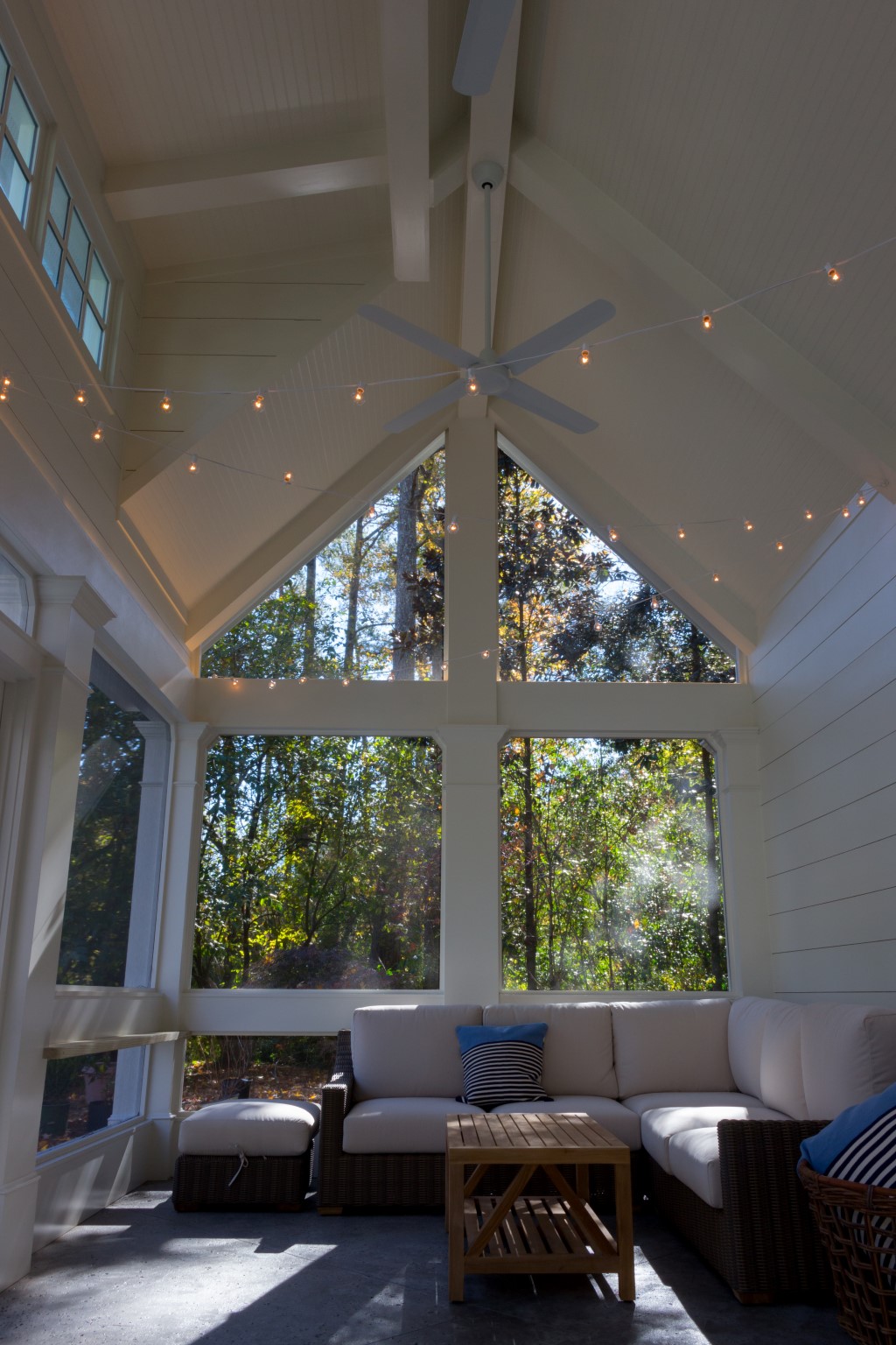 The inside of a small pool house with large windows, string lights, and furniture