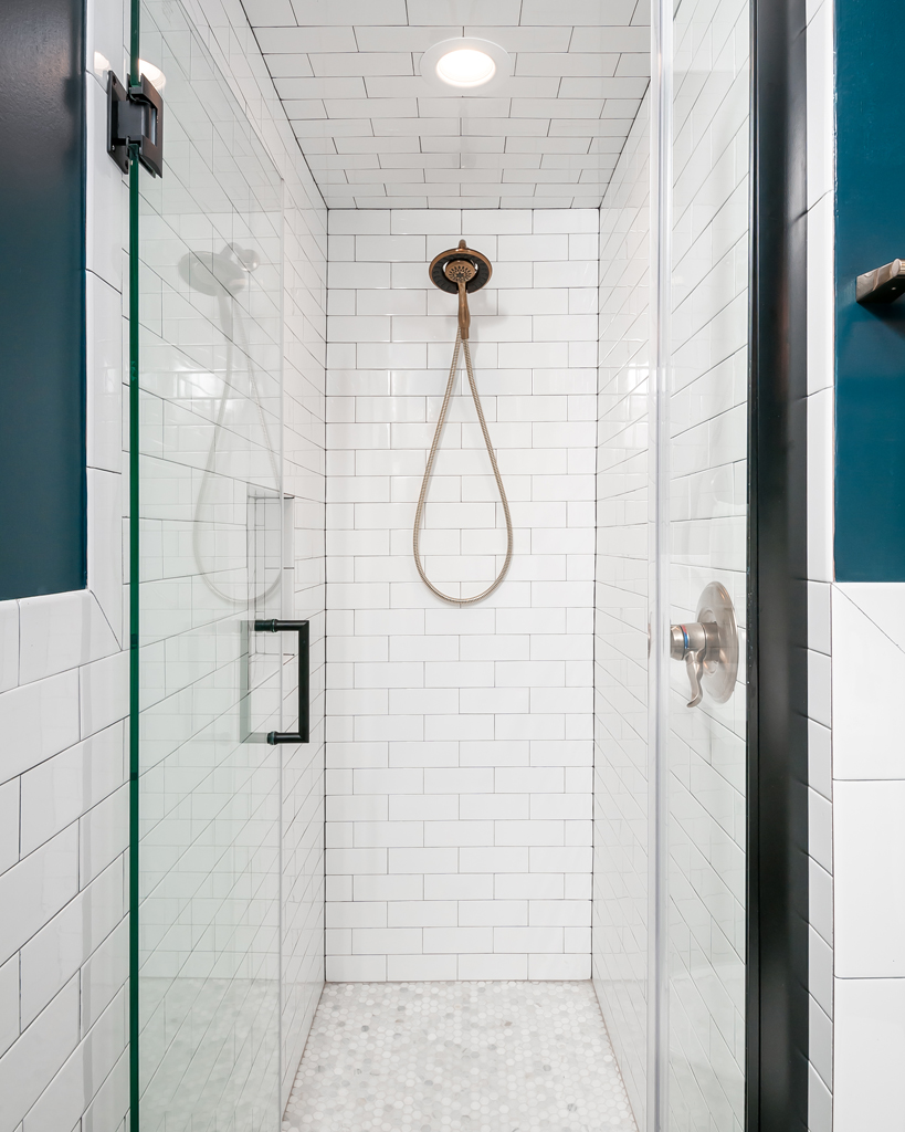 a walk in shower with a white tiled wall and a glass door