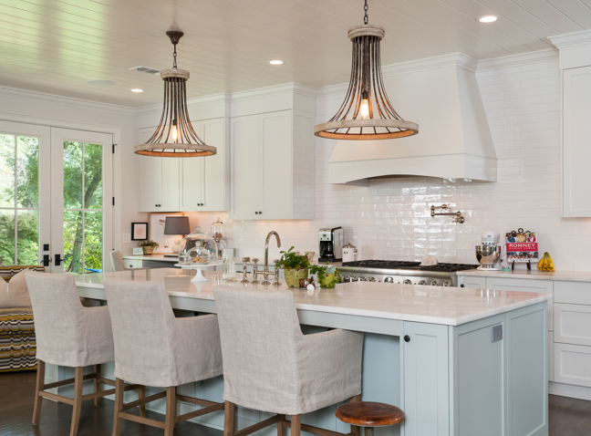 a large white kitchen with unique light fixtures and a center island surrounded by chairs