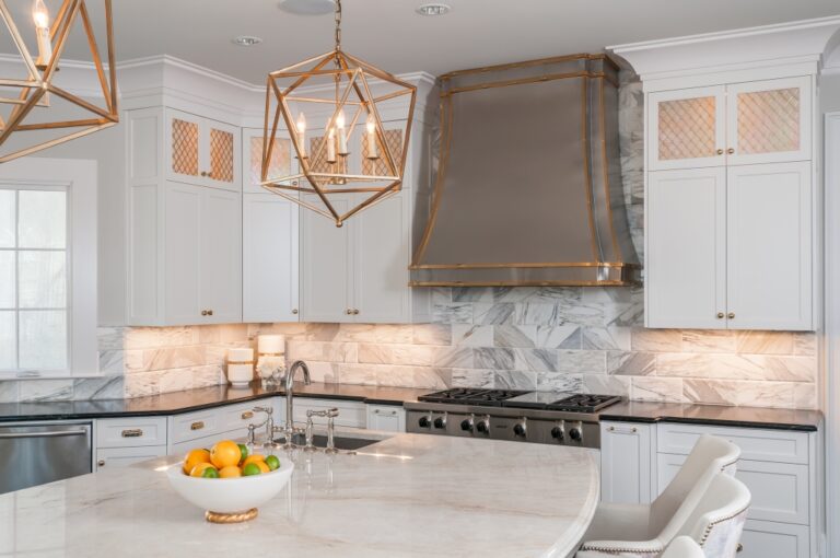a kitchen with dark marble counter tops, an island, gold light fixtures, and white cabinets