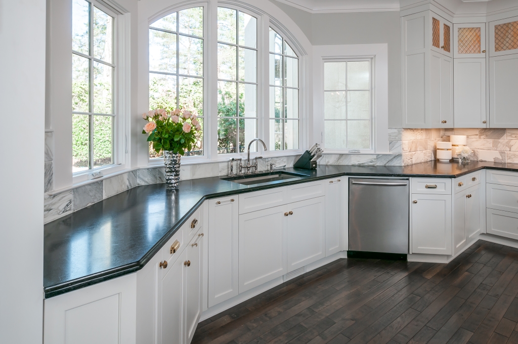a kitchen with white cabinets, black counter tops, and a large picture window above the sink