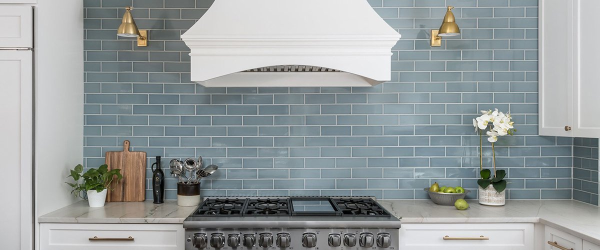 Kitchen oven & gas range with blue subway tile backsplash and gold sconces