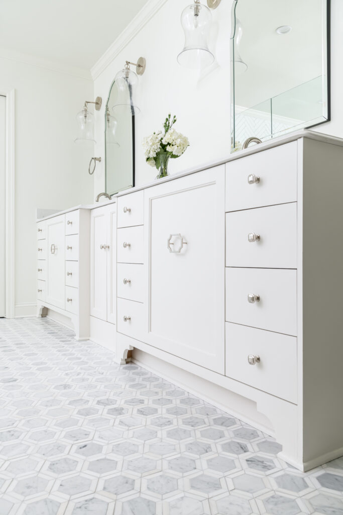 a bathroom with two large mirrors, white cabinets, and marble tiled floors