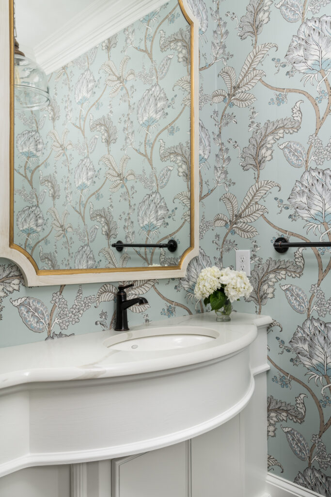 a white sink sitting under a mirror in a bathroom with light blue floral wallpaper